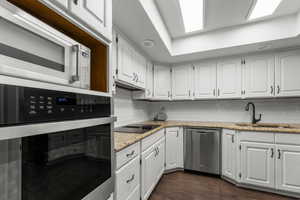 Kitchen with dark wood-type flooring, a sink, white cabinets, appliances with stainless steel finishes, and decorative backsplash