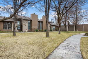 Mid-century modern home with brick siding, a front lawn, a chimney, and fence