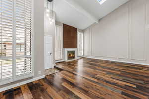 Unfurnished living room with visible vents, dark wood finished floors, beam ceiling, and a glass covered fireplace