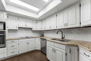 Kitchen with dark wood-style floors, stainless steel appliances, white cabinets, a sink, and light stone countertops