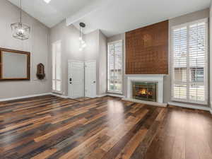 Unfurnished living room featuring a chandelier, dark wood-style flooring, baseboards, beam ceiling, and a glass covered fireplace