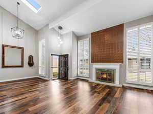 Unfurnished living room featuring dark wood-style floors, a skylight, visible vents, a glass covered fireplace, and baseboards