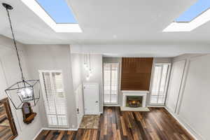 Unfurnished living room with a lit fireplace, baseboards, and dark wood-style flooring