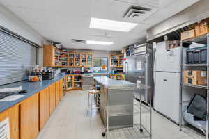 Kitchen featuring a paneled ceiling, dishwasher, light tile patterned flooring, white fridge, and a kitchen bar