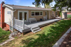 Back of property featuring a chimney, french doors, a  deck, and a yard