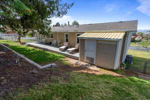 Rear view of property featuring a yard, fence, a deck, and an outbuilding