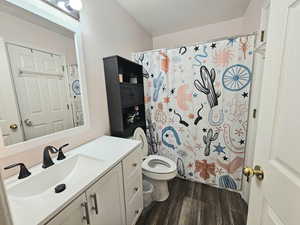 Bathroom with toilet, curtained shower, wood finished floors, and vanity