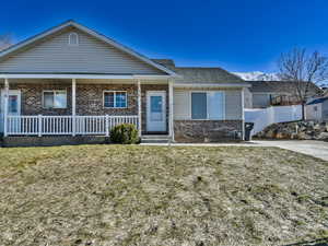 View of front of home with covered porch, brick siding, a front yard, and fence