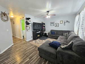 Living room with baseboards, ceiling fan, wood finished floors, a textured ceiling, and a fireplace