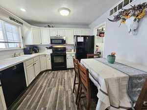 Kitchen with dark wood-style flooring, recessed lighting, light countertops, a sink, and black appliances