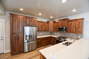 Kitchen with sink, tasteful backsplash, stainless steel appliances, and light hardwood / wood-style flooring