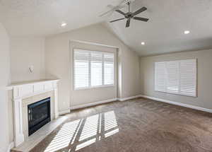 Unfurnished living room with a tile fireplace, vaulted ceiling, a textured ceiling, and light colored carpet