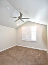 Spare room featuring vaulted ceiling, ceiling fan, carpet flooring, and a textured ceiling