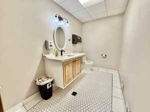 Bathroom with toilet, a paneled ceiling, tile patterned floors, and vanity