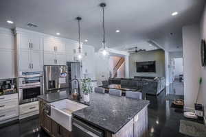 Kitchen featuring appliances with stainless steel finishes, open floor plan, white cabinetry, and a center island with sink