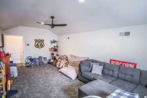 Living room featuring dark carpet, ceiling fan, visible vents, and vaulted ceiling