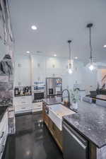 Kitchen with decorative light fixtures, appliances with stainless steel finishes, white cabinets, an island with sink, and dark stone counters