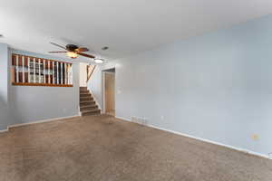 Front room featuring ceiling fan, stairs, visible vents, and baseboards