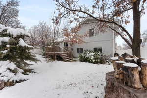 Snow covered house featuring a garage, fence, and a wooden deck