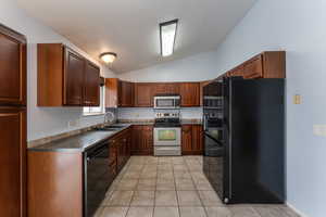 Kitchen featuring dark countertops, black appliances, a sink, and lofted ceiling