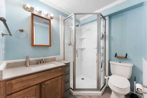 Bathroom with crown molding, toilet, a shower stall, vanity, and wood finished floors