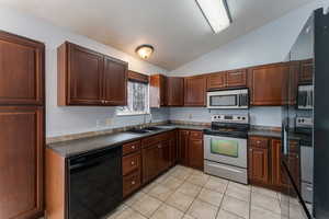 Kitchen with lofted ceiling, light tile patterned flooring, a sink, appliances with stainless steel finishes, and dark countertops