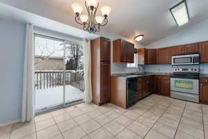 Kitchen with dark countertops, appliances with stainless steel finishes, light tile patterned flooring, vaulted ceiling, and a sink.