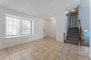 Living room featuring light tile patterned floors, vaulted ceiling, and stairs