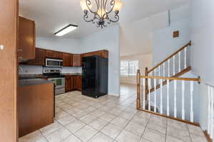 Kitchen featuring stainless steel appliances, dark countertops, decorative light fixtures, and light tile patterned flooring