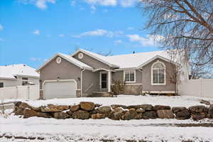 View of front of house with a garage, stone siding, fence, and stucco siding