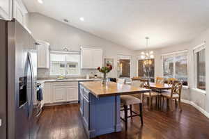 Kitchen featuring decorative light fixtures, appliances with stainless steel finishes, white cabinetry, a kitchen island, and wood counters