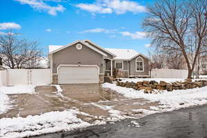 Ranch-style house featuring an attached garage, stone siding, fence, and stucco siding