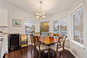 Dining area with wine cooler, dark wood finished floors, vaulted ceiling, a chandelier, and baseboards