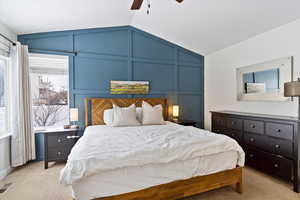 Bedroom with lofted ceiling, light carpet, visible vents, and a decorative wall