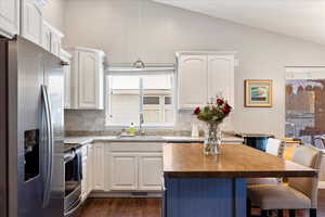 Kitchen with lofted ceiling, a kitchen island, wood counters, stainless steel appliances, and white cabinetry