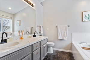 Bathroom with marble finish floor, double vanity, a sink, baseboards, and a bath