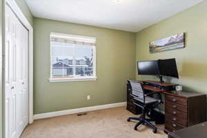 Office area featuring light carpet, visible vents, baseboards, and a textured ceiling