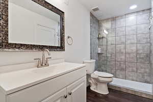 Bathroom with a walk in shower, toilet, wood finished floors, vanity, and visible vents