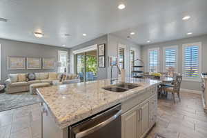 Kitchen with a center island with sink, sink, light stone counters, a textured ceiling, and stainless steel dishwasher