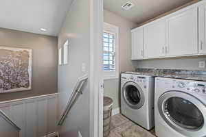 Clothes washing area featuring light tile patterned floors, washer and clothes dryer, and cabinets