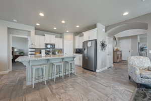 Kitchen with white cabinetry, a kitchen island with sink, stainless steel appliances, a breakfast bar, and light stone counters