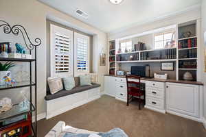 Carpeted office space with a healthy amount of sunlight and built in desk