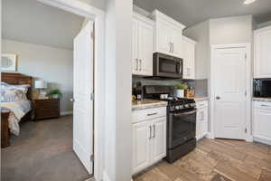 Kitchen with white cabinetry, range with gas cooktop, light stone countertops, tasteful backsplash, and black microwave