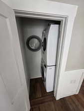 Clothes washing area with dark wood-type flooring and stacked washer and dryer