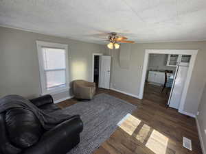 Living area with visible vents, a textured ceiling, baseboards, and dark wood-style flooring