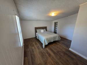 Bedroom featuring baseboards, a textured ceiling, wood finished floors, and wooden walls