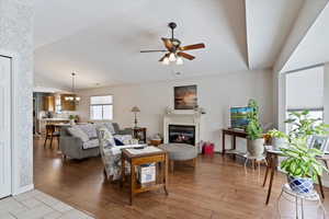 Living room with wood laminate floors, baseboards, ceiling fan with light, and fireplace