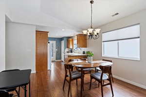 Dining space with large window, a chandelier, vaulted ceiling, and wood-style flooring