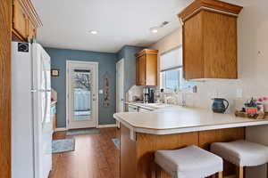 Kitchen featuring a peninsula, a sink, white countertops, freestanding refrigerator, and wood finished floors