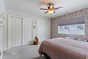 Primary bedroom with two closets, light colored carpet, ceiling fan, and a textured ceiling